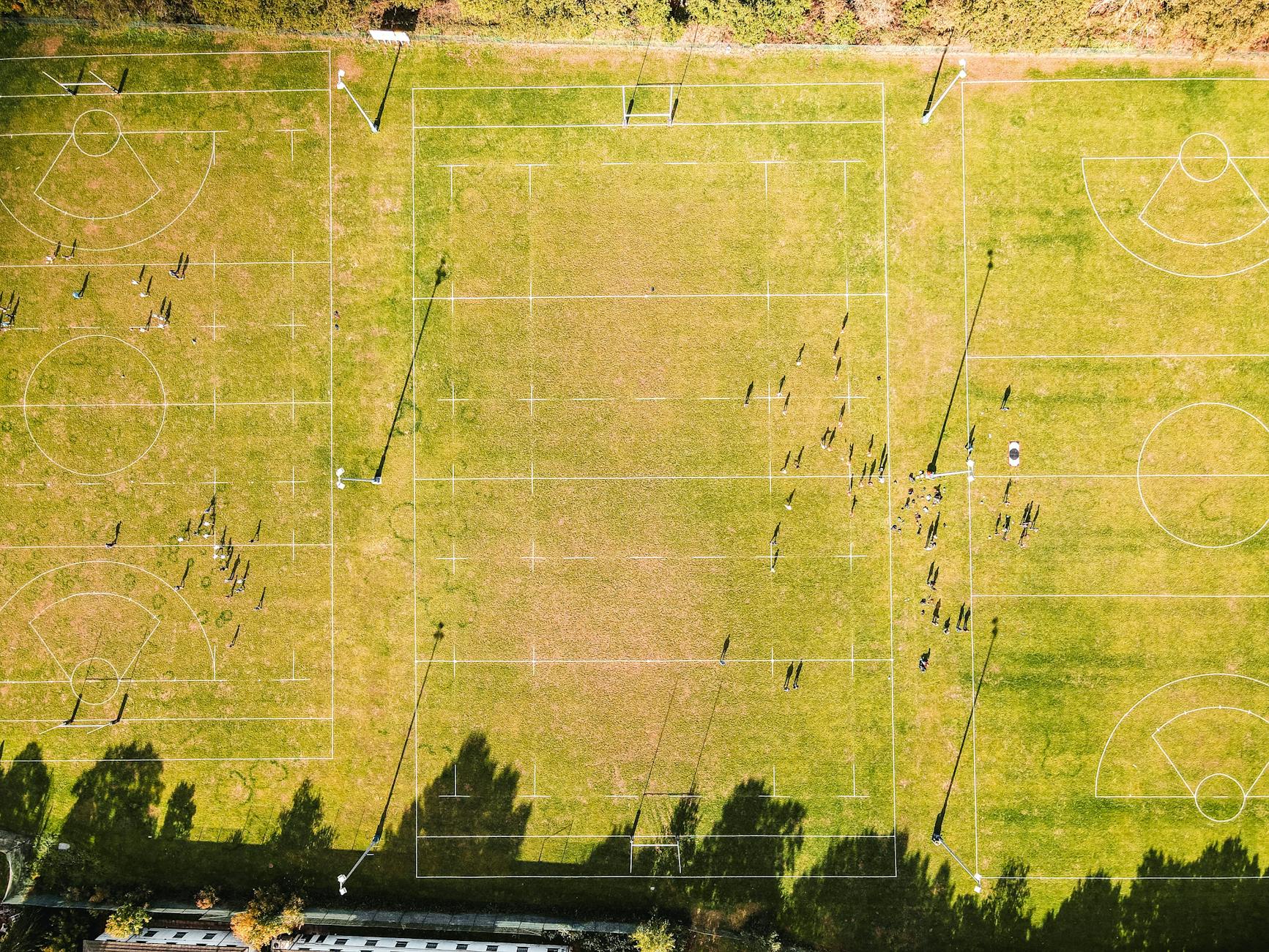 Drone view of teams of anonymous sportspeople playing rugby on green fields on sunny day